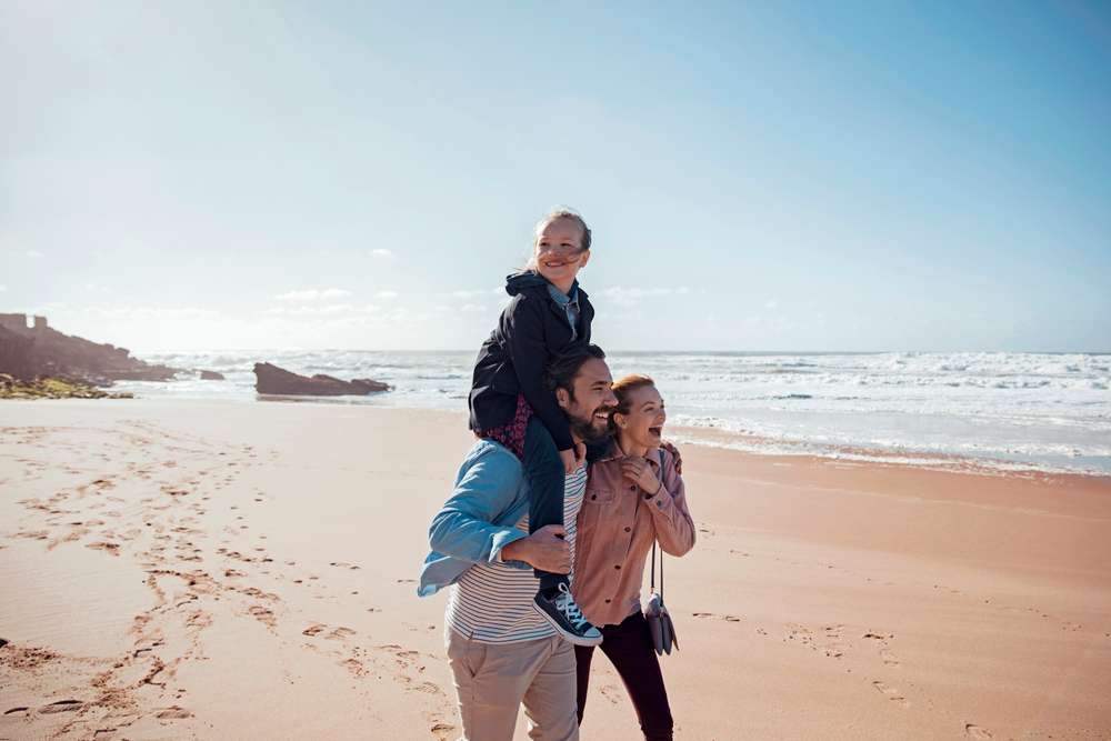 Glad familj på en blåsig strand som njuter av att vara utomhus tillsammans.